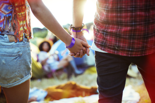 Close up of couple holding hands outside tents at music festival